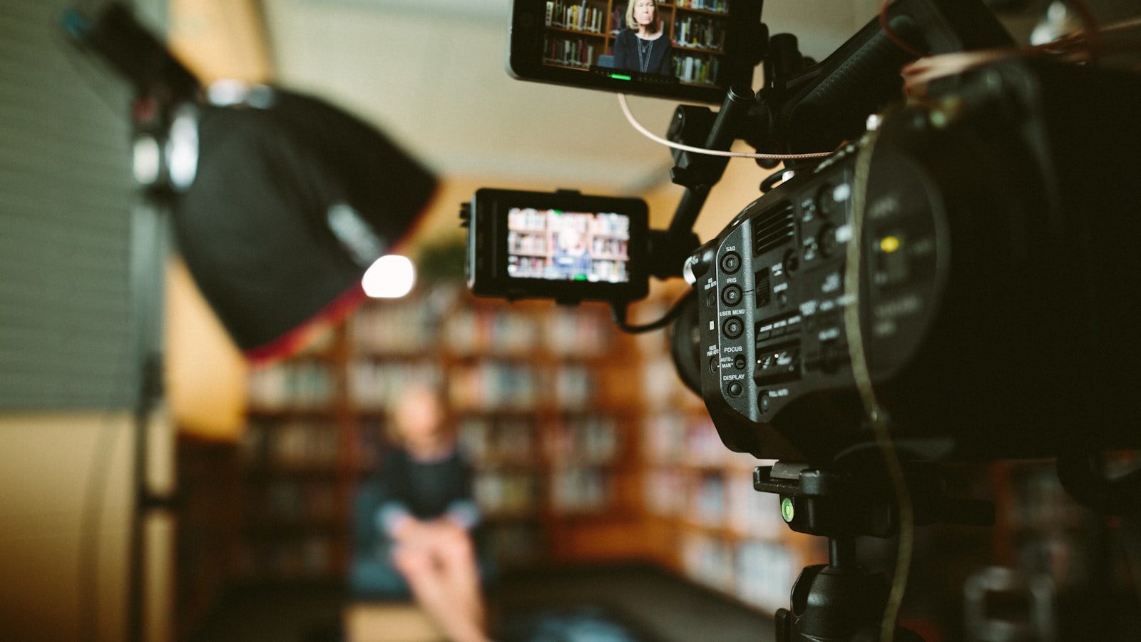 Tournage d'une interview : caméra et écran de contrôle face à l'intervenante, devant une bibliothèque